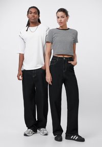 Svart vide bukser med kontrasterende sømmer, kombinert med en hvit oversized t-skjorte og en svart-hvitt stripete cropped topp.