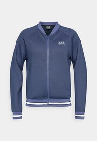 Marineblauwe zip-up jas van textiel met een geribbelde stof, geribbelde manchetten en zoom, met witte accentstrepen en een cirkelvormig logo op de borst.