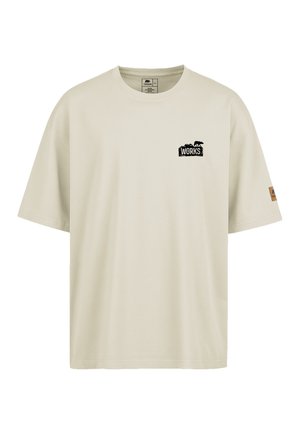 Lichtbeige katoenen t-shirt met een ronde hals, losse pasvorm, logo in het zwart op de linkerborst en een klein bruin label op de rechtermouw.