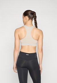 Bežs sporta krūšturis ar racerback dizainu, izgatavots no gludas auduma. Apvienots ar melniem augsta vidukļa legingiem ar teksturētu jostas daļu.