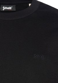 Schwarzer Pullover aus geripptem Material mit klassischem Rundhalsausschnitt und dezentem, tonalem "Schott"-Logo auf der Brust. Weicher Stoff.