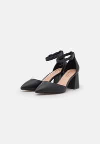 Black leather high-heeled shoes with a pointed toe, adjustable ankle strap, and a block heel. Smooth texture with a minimal design.