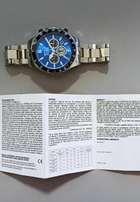 Orologio cronografo in acciaio inox silver con quadrante blu, lunetta nera, dettagli argentati e bracciale a maglie. Include manuale di istruzioni e garanzia.