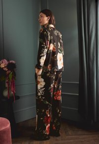 Černý pyžamový set s květinovým vzorem vyrobený z měkké látky, s ležérním střihem, dlouhými rukávy a širokými kalhotami, zdobený barevnými květinami.