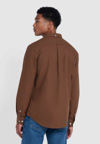 Bruine blouse met lange mouwen en knoopmanchetten, voorzien van een enkele rugplooi, gemaakt van gladde stof, gecombineerd met blauwe jeans in een casual pasvorm.