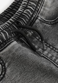 Tela de mezclilla gris con una textura ligeramente descolorida. Presenta una cintura elástica con un cordón negro y puntas metálicas.