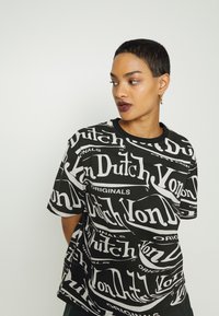 Black t-shirt featuring white graphic text that reads "Von Dutch" and "Originals" in varying styles and orientations. Short sleeves, round neckline.