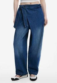 Denimwrapbyxor i mörkblått. Har en knytbar midja och lös passform. Materialet har en urtvättad textur, med raka ben och fickor.