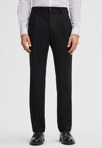 Schwarze Hosen aus strukturiertem Stoff, mit einem Knopfverschluss, zwei vorderen Taschen und einem geraden Bein Design. Getragen mit einem weißen Hemd.