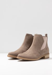 Tan suede ankle boots with elastic side panels, low stacked heel, and rounded toe. Features a smooth texture and minimalistic design.