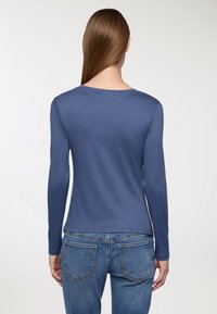 Koszula z długim rękawem w jednolitym niebieskim kolorze, wykonana z gładkiego, elastycznego materiału, z okrągłym dekoltem i dopasowanym krojem.