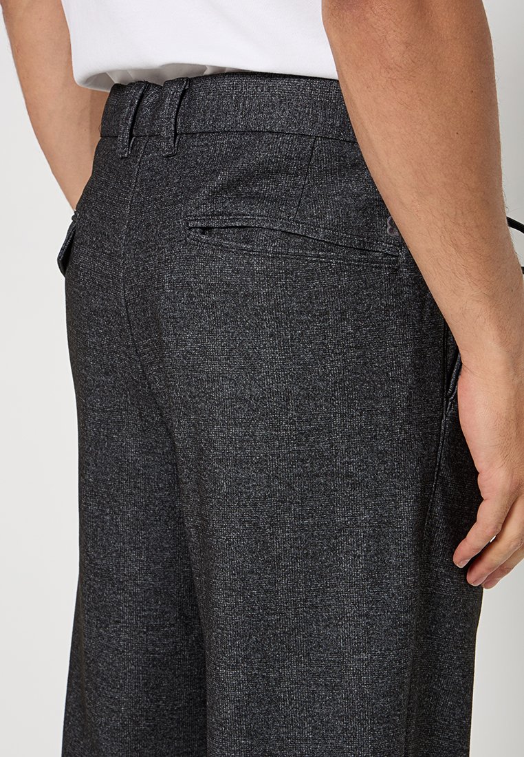 Grau gewebte Hose mit glatter Textur, seitlichen Taschen und einem enganliegenden Taillenbund. Die Rückansicht zeigt Details des Taschendesigns und des Stoffes.