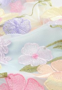 Broderad genomskinlig tyg med pastellfärger av blommor i lavendel, rosa och persika med gröna blad på en ljusblå bakgrund. Mjuk textur.