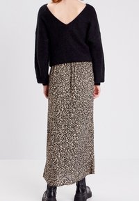 Svart löst stickad tröja med djup V-rygg, i kombination med en lång blommig kjol med små vita blommor på en mörk bakgrund. Svarta stövlar.