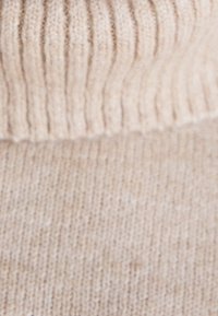 Gros plan sur un tissu en tricot beige doux avec une texture côtelée en haut et un motif de tricot lisse en dessous.