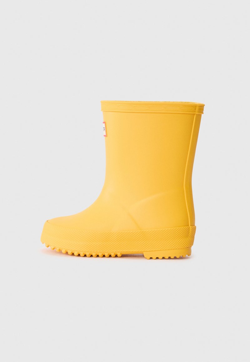 Bota de chuva amarela de borracha com fundo texturizado e superfície lisa. Apresenta um bico redondo e uma parte superior curta e arredondada.
