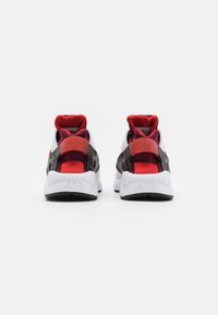 Zwarte en rode Nike sneakers met een witte zool, voorzien van een gevoerde kraag, bovenkant van mesh en een prominent "AIR" logo op de hiel.