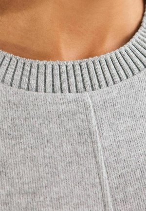 Gros plan sur un col présentant un pull en maille côtelée gris clair avec une couture verticale au centre.