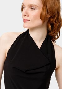 Top negro tipo halter con un diseño drapeado y textura suave, que cuenta con un escote cruzado y hombros al aire.