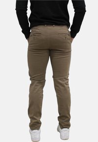 Khaki slim-fit broek met ritszakken aan de achterkant, gemaakt van een katoenmix en met een gladde textuur; gedragen met witte sneakers en een zwart shirt.