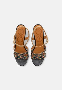 Tiras multicolores tejidas en verde, amarillo y burdeos sobre sandalias de cuero negro texturizado, con una plantilla color canela y tira al tobillo.