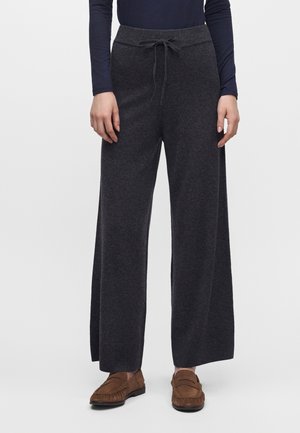Modèle portant un pantalon ample anthracite à taille coulissée, un haut foncé et des mocassins marron.
