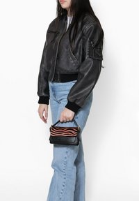 Veste bomber cropped en cuir noir avec des poignets côtelés, associée à un jean taille haute bleu clair. Petit sac avec des rayures ondulées noires et oranges.