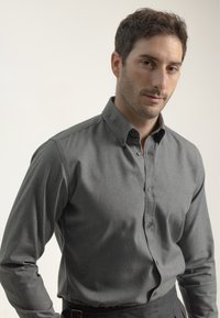 Camisa gris de botones hecha de tejido texturizado, con cuello estándar, mangas largas y botones oscuros, combinada con pantalones oscuros.