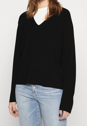 Maglione nero a costine con scollo a V e maniche lunghe, caratterizzato da una vestibilità morbida e tessuto testurizzato, abbinato a jeans di denim blu chiaro.