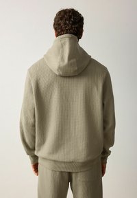 Sudadera con capucha en verde olivo claro, fabricada en tejido texturizado, con detalles acanalados, corte relajado y puños de banda, acompañada de pantalones a juego.