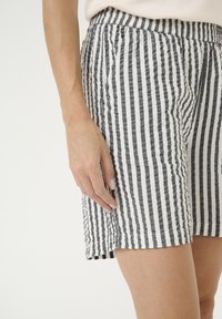 Pantaloni corti a righe bianche e nere in tessuto strutturato, con una vestibilità comoda, vita elastica e tasche laterali.