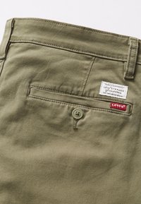 Poche arrière d'un pantalon Levi's vert olive avec fermeture à bouton et étiquettes en tissu blanc et rouge de marque Levi's.