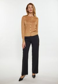 Brauner, strukturiertes cardigan mit rundem Halsausschnitt und Knopfverschluss, kombiniert mit schwarzen weit geschnittenen Hosen und spitzen schwarzen Schuhen.