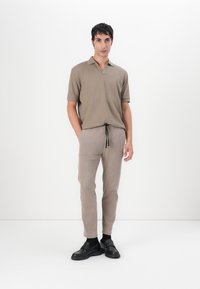 Beige polo tričko s výstřihem do V, krátkými rukávy a texturovanou látkou; v kombinaci se světle béžovými kalhotami s tkaničkou. Černé boty včetně.