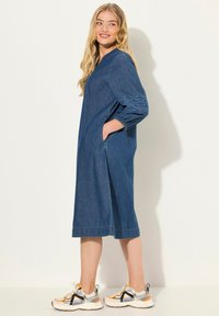 Denimivuori mekko V-pääntiellä, kolmannes hihapituus, jossa on brodeerattuja yksityiskohtia, sivutaskut ja rento istuvuus. Yhdistetty urheilullisiin lenkkareihin.