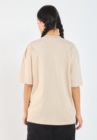 Camiseta de gran tamaño en beige con mangas cortas, fabricada en un tejido suave. Presenta un escote redondo y un diseño simple, sin adornos.