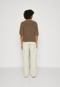 Maglione a maniche corte marrone in maglia con scollatura rotonda, abbinato a pantaloni bianchi a gamba larga. Morbida texture e vestibilità rilassata.