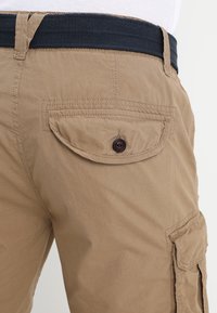 Beige cargo šortky s tkaným námořnickým opaskem, zapínací zadní kapsou a texturovanou látkou s hladkým povrchem.