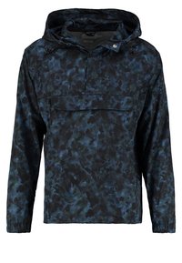 Veste anorak dans un motif tie-dye bleu foncé, fabriquée en matériau léger avec une capuche, une poche avant et des poignets élastiques.
