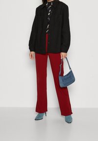 Zwarte textuurjasje, gebloemd blouse, rode broek, blauwe haklaarzen en een kleine blauwe handtas. De outfit heeft verschillende complementaire kleuren.