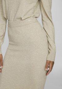 Vestido de punto beige con una cintura ajustada, mangas largas y una textura suave, con sutiles acentos acanalados en los puños y el dobladillo.