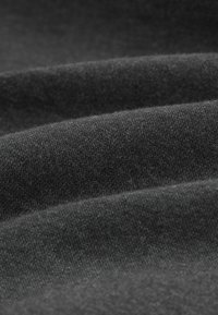 Tmavě šedá tkanina s měkkým, strukturovaným povrchem, s jemnými vlákny a jemnými variacemi odstínu, uspořádaná v hladkých, vlnitých záhybech.