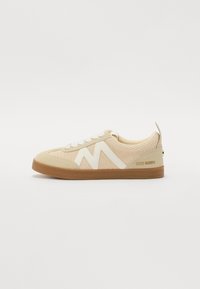 Sneaker beige con tomaia in maglia testurizzata, dettagli in gomma bianca e suola in gomma marrone. Presenta un design con lacci e il logo sul tallone.