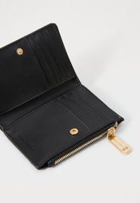 Portefeuille en cuir noir avec fermeture éclair, plusieurs emplacements pour cartes, quincaillerie dorée et logo. Texture lisse avec des accents surpiqués. Vue ouverte.