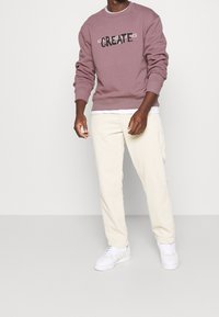 Sweatshirt violet clair avec "CREATE" en texte noir, associé à un pantalon en velours côtelé crème et des baskets blanches. Texture lisse.