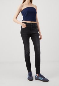 Top sin mangas de mezclilla oscura combinado con jeans negros ajustados y zapatillas adidas azules con tres rayas de color azul claro.