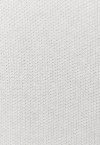 Weißer gestrickter Stoff mit einem strukturierten Muster und kleinen, gleichmäßigen Stichen, die ein weiches und leichtes Erscheinungsbild verleihen.