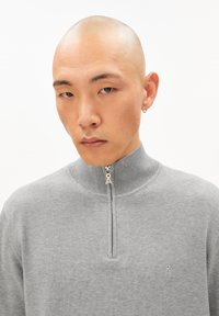 Grauer Pullover mit Reißverschluss aus strukturiertem Stoff. Verfügt über einen hohen Kragen und ein kleines Logo auf der Brust. Der Reißverschlussanhänger hat ein unverwechselbares Design.