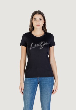 Zwarte katoenen t-shirt met een glinsterend "Live Go" tekstontwerp, korte mouwen en een ronde hals, gecombineerd met blauwe jeans.