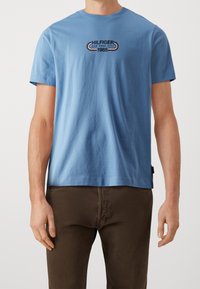 Jasnoniebieska koszulka z krótkim rękawem wykonana z bawełny, z graficznym logo w ciemnoniebieskim, czerwonym i białym kolorze z napisem "HILFIGER NEW YORK CITY 1985".